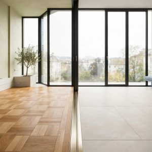 Parquet en chêne et carrelage clair se rejoignent près d’une grande baie vitrée.